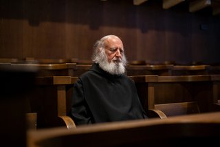 Pater Anselm Grün sitzt in einer Kirchenbank, er ist im Gebet vertieft. 