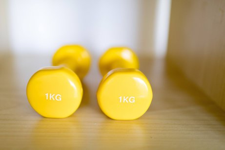 Rehabilitation mit Sport Zwei gelbe Ein-Kilo-Hanteln liegen auf einem Holzboden