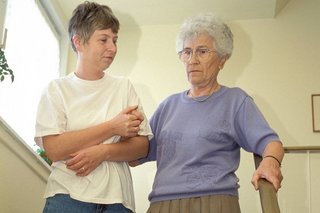 Eine jüngere Frau hilft einer Seniorin, eine Treppe hinabzugehen. Sie hält die ältere Frau am Arm eingehakt fest.