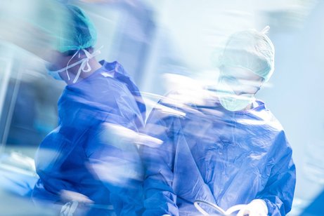 Operation im Krankenhaus Verschwommene Aufnahme zweier männlicher Chirurgen während einer Operation, sie tragen blaue OP-Kleidung