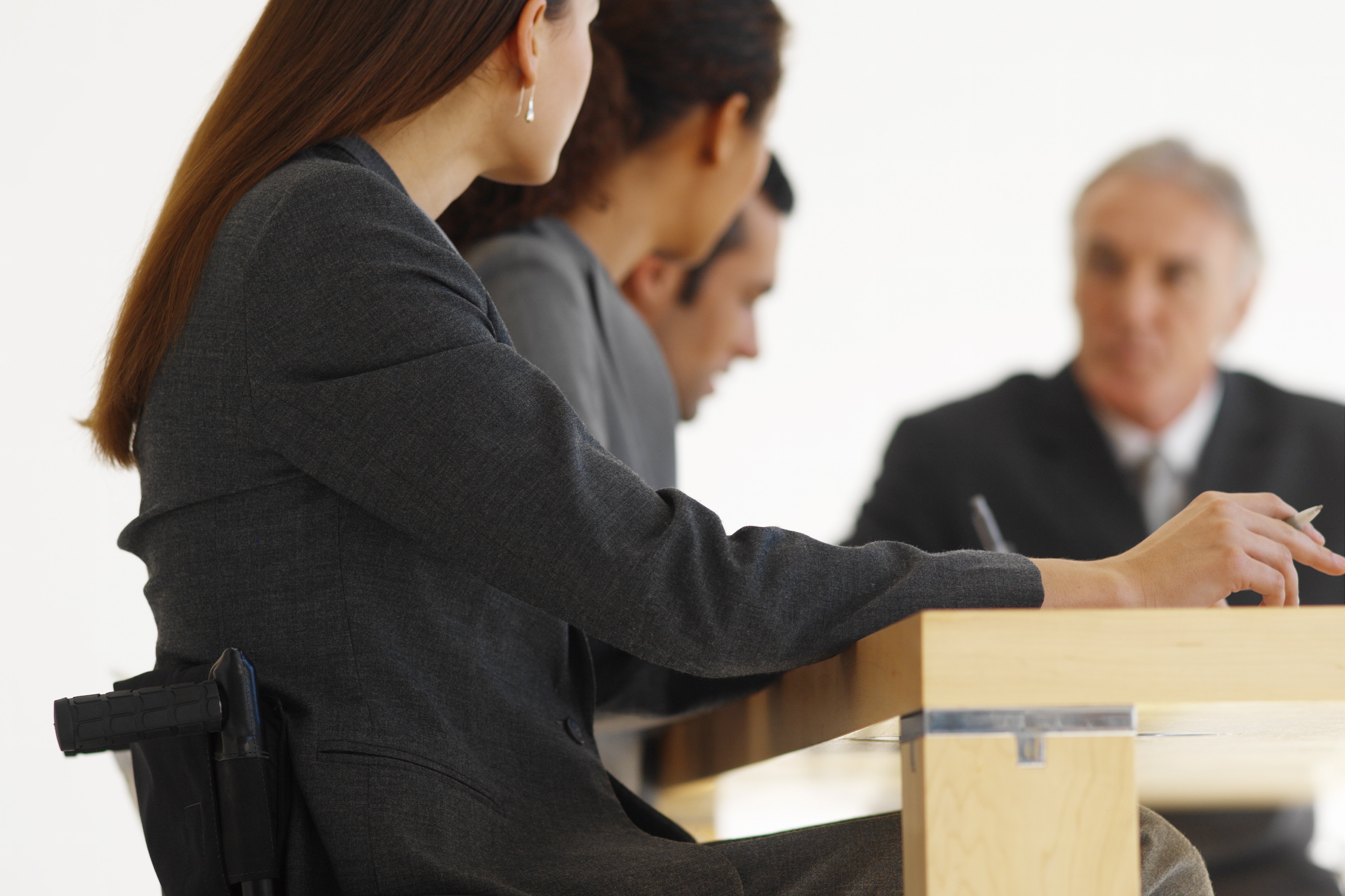 Leute in Business-Kleidung gemeinsam an einem Tisch, eine Frau sitzt im Rollstuhl