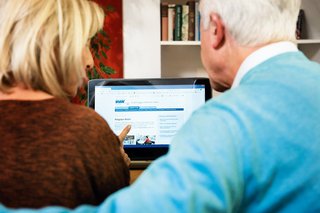Ein älteres Paar am Computer, auf dem Bildschirm sieht man die Facebook-Seite des VdK Deutschland