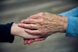 Die Hand einer älteren Frau hält die Hand einer jüngeren Frau in einer tröstenden Geste.