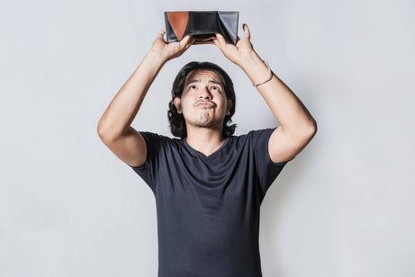 Geldmangel Ein Mann hält seine leere Brieftasche umgedreht über den Kopf, er schaut mit traurigem Gesichtsausdruck, ob etwas herausfällt.