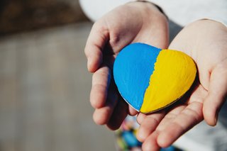 Ein kleines Kind hält einen herzförmigen Stein, der in den Farben der ukrainischen Flagge (blau und gelb) bemalt ist.