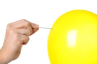 Ein gelber Luftballon, jemand hält eine Nadel daran, um ihn zum Platzen zu bringen