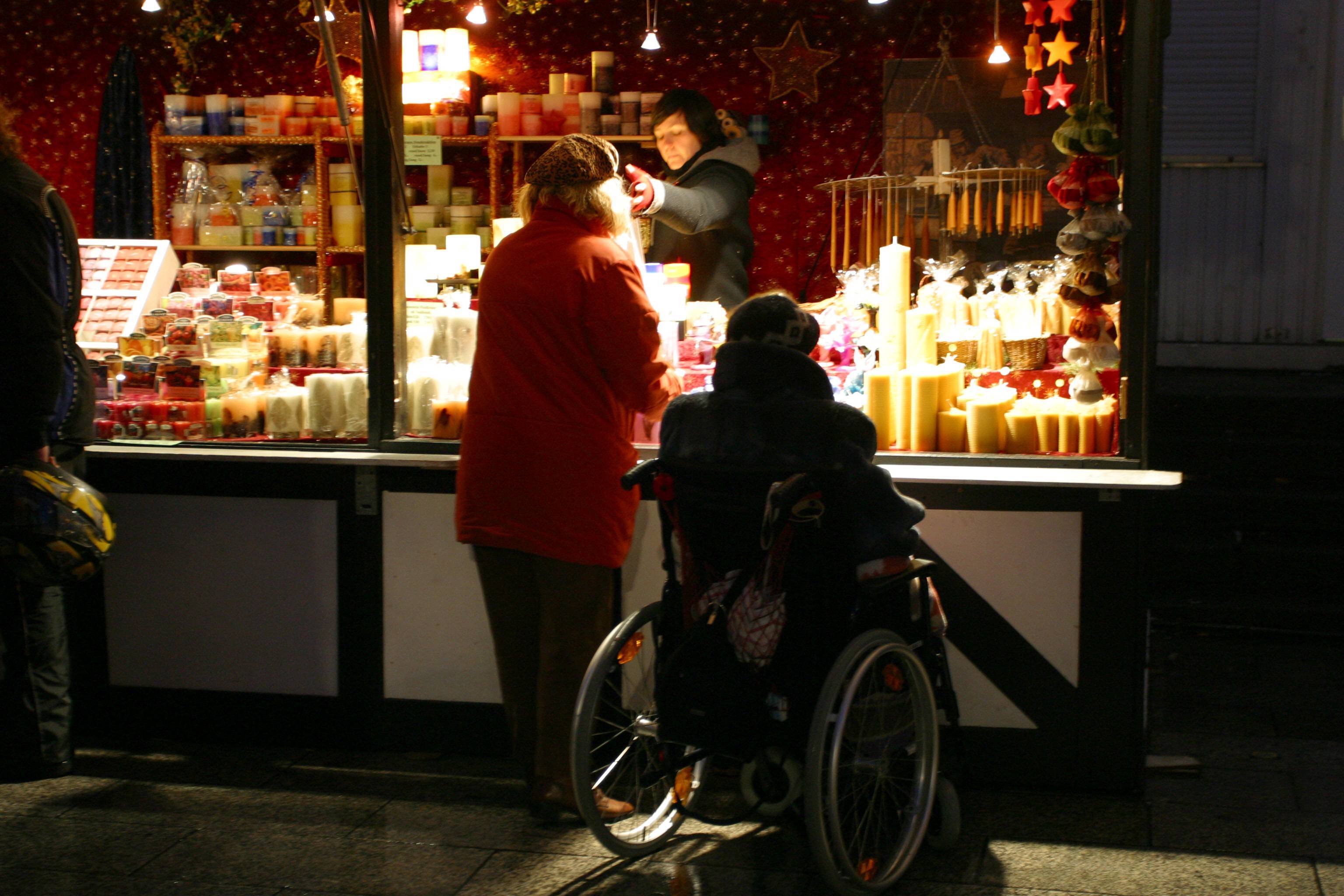 Weihnachtsmarkt Ein älterer Mann im Rollstuhl und eine ältere Frau an einem Kerzenstand auf dem Weihnachtsmarkt am Breitscheidplatz in Berlin