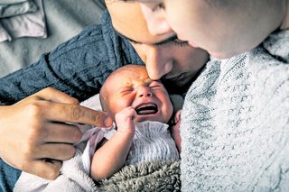 Ein schreiendes Baby in den Armen der Eltern.