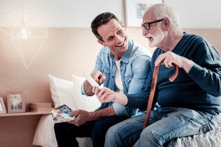 Vater und Sohn sitzen auf den Pflegebett und reden miteinander.