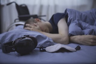 Eine Person liegt im Dunkeln im Bett, daneben Kopfhörer und Schlafmaske