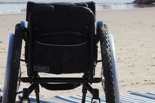 Ein leerer Rollstuhl am Strand, daneben ein Strandtuch