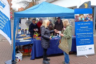 VdK-Ehrenamtliche zusammen mit Interessierten am blauen VdK-Infostand in Uelzen im März 2024