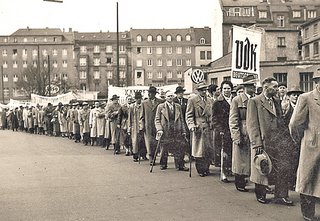 Ein schwarz-weiß Foto von einer langen Schlangen von Männern, die Hüte und Mäntel tragen.