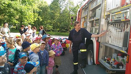 Kinder stehen mit Feuerwehrmann am Feuerwehrauto