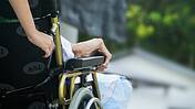 Das Bild zeigt, wie eine Person im Rollstuhl voneiner Pflegekraft geschoben wird.