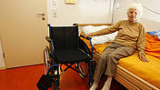 Symbolfoto: Seniorin in einem Pflegeheim sitzt auf der Bettkante, neben ihr ein Rollstuhl