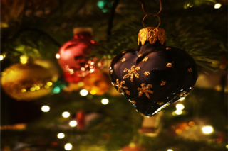 Im warmen Glanze erstrahlen die verschieden bunten Kugeln und Anhänger am Weihnachtsbaum. Im Mittelpunkt des Bildausschnitts, funkeln golden die Sterne auf dem blauen Glasherz.