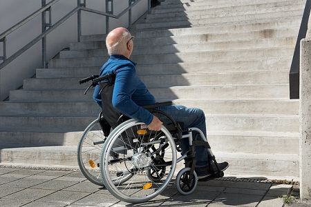 Ein Mann mit Rollstuhl steht vor einer langen Treppe
