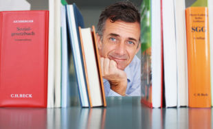 Ein Mann sieht hinter einem Bücherstapel hervor
