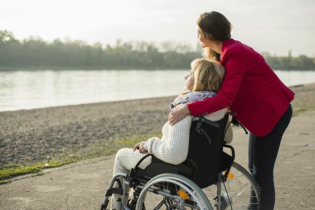 Foto: junge Frau umarmt eine ältere Frau im Rollstuhl