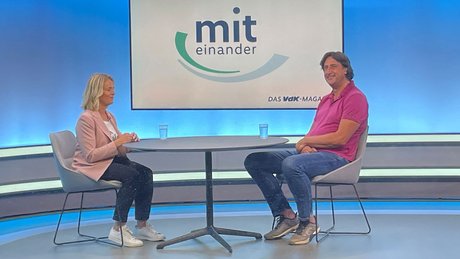 Verena Bentele und Christian Schenk sitzen im TV-Studio von "Miteinander" gegenüber an einem Tisch und unterhalten sich.