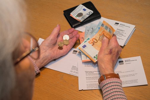  Alte Frau mit Rentenbescheid, auf dem Tisch liegen außerdem Geldscheine und Münzen