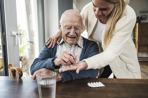 Frau gibt ihrem alten Vater seine Tabletten zur Einnahme.