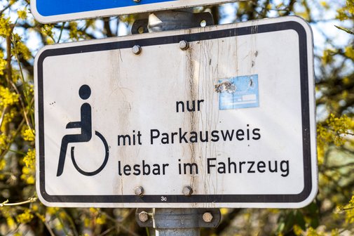Ein Verkehrsschild an einem Behindertenparkplatz mit einem Rollstuhl-Symbol und dem Text "nur mit Parkausweis lesbar in Fahrzeug".