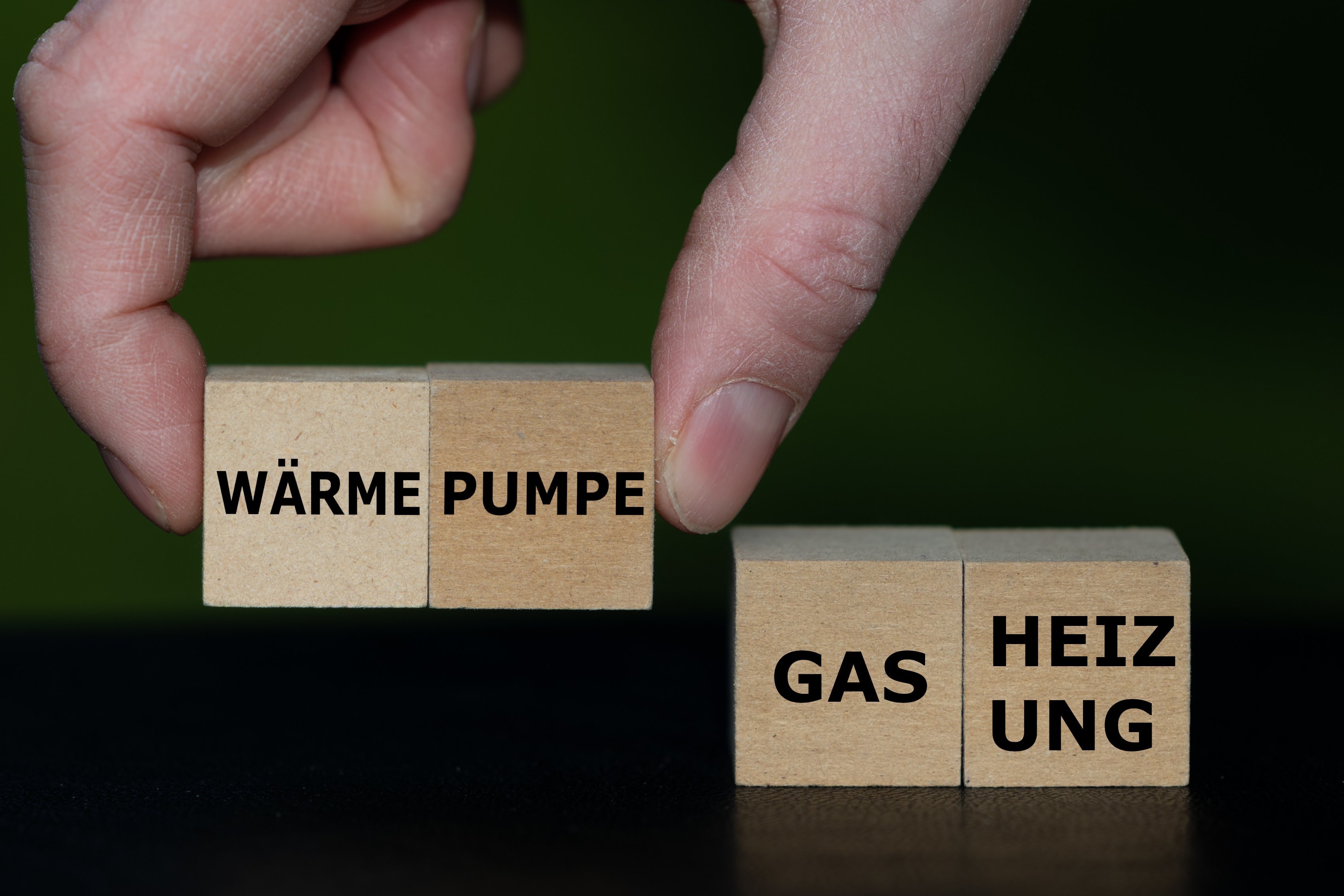 Wärmepumpe oder Gasheizung Eine Hand setzt Holzwürfel mit Wörtern zusammen, sie bilden die Worte "Wärme-Pumpe" und "Gas-Heizung"