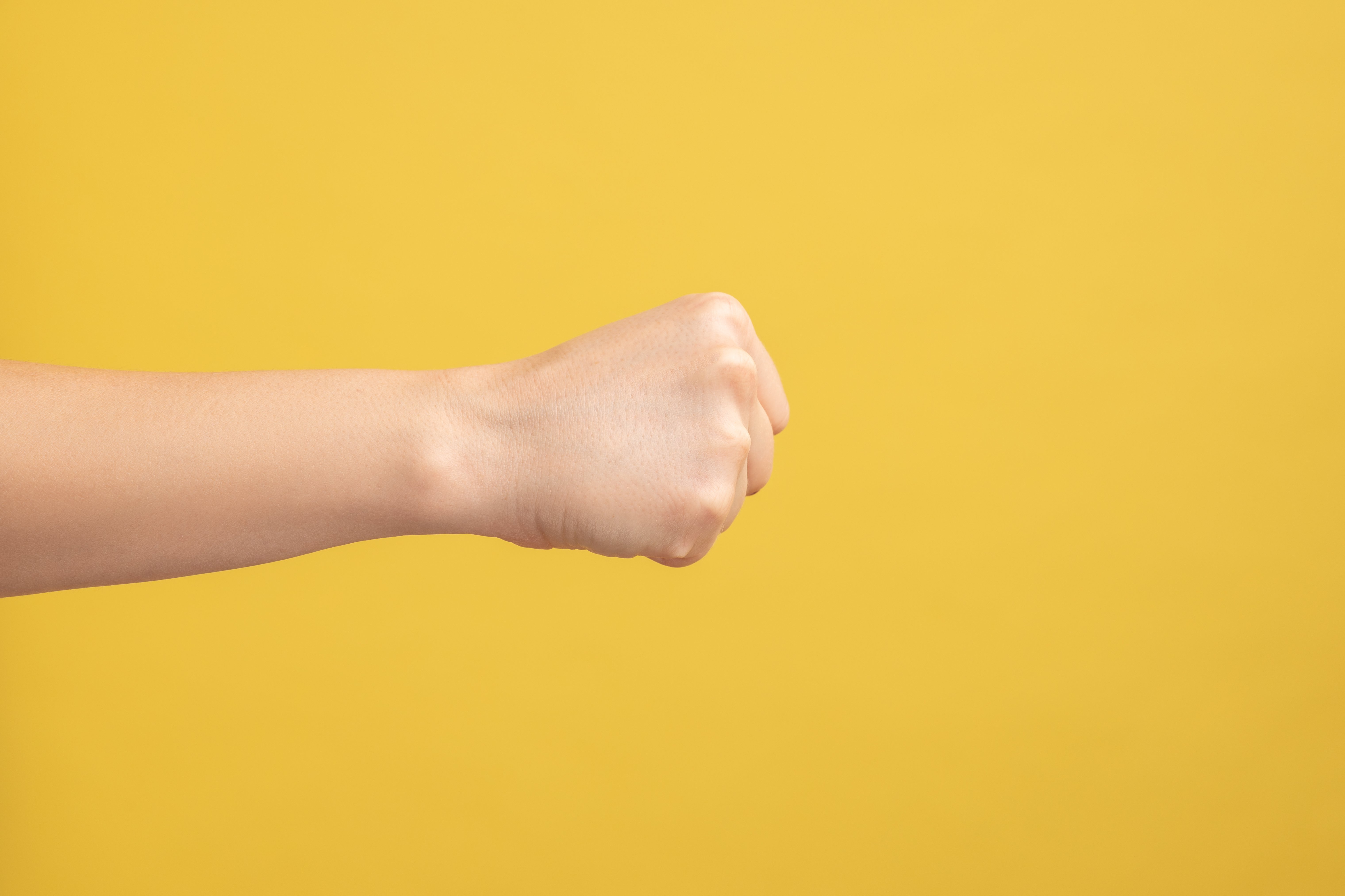 Gewalt Das Foto zeigt einen ausgestreckten Arm mit geballter Faust vor gelbem Hintergrund.