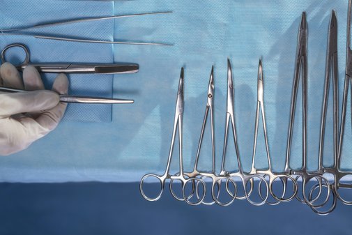 Operations-Besteck Hand eines Chirurgen nimmt chirurgische Instrumente, die nebeneinander aufgereiht auf einem Tuch liegen