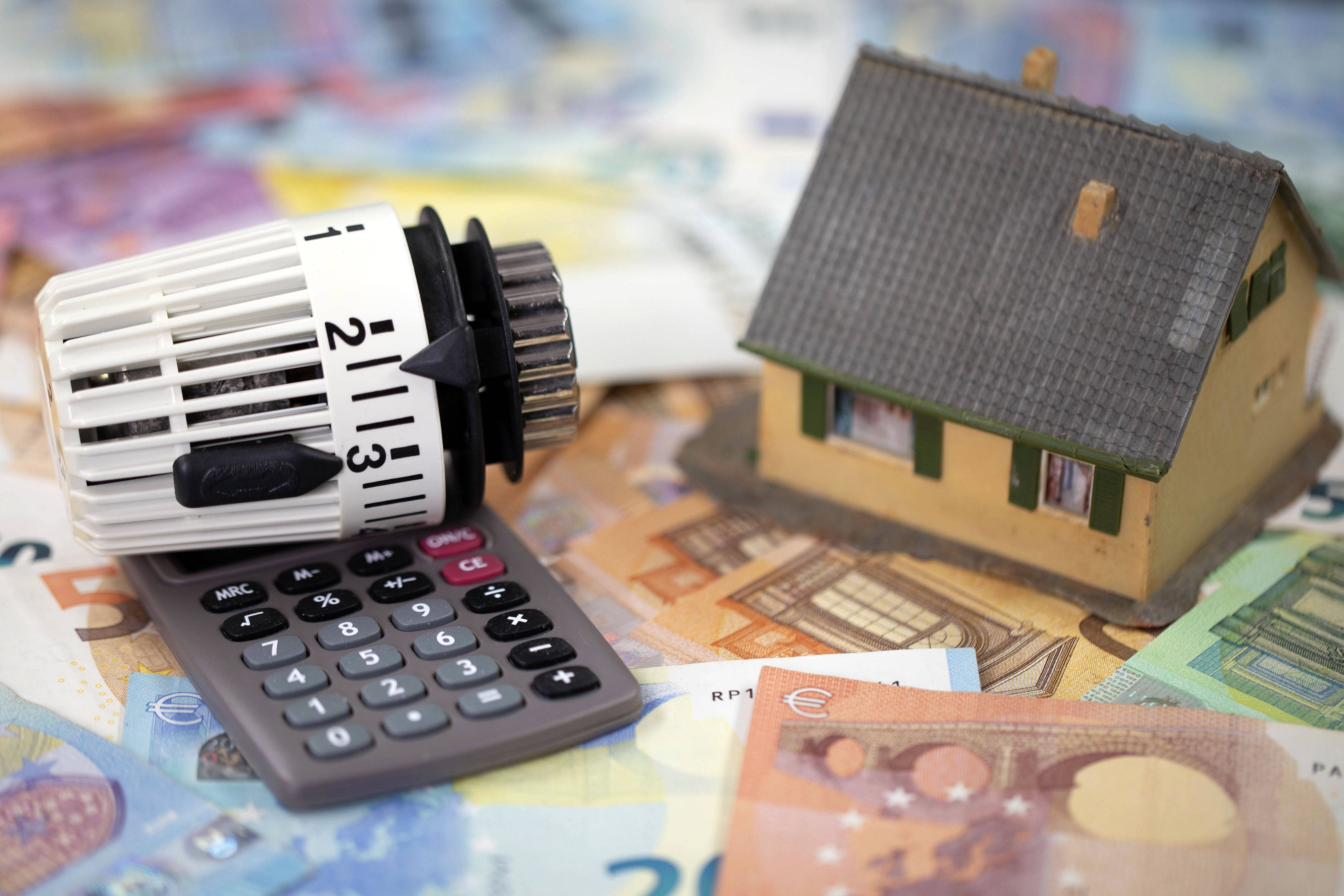 Heizungstausch mit finanziellen Zuschüssen Ein Spielzeughäuschen, ein Taschenrechner und ein Heizungsthermostat liegen auf Geldscheinen als Symbol für finanzielle Zuschüsse beim Gebäudeenergiegesetz