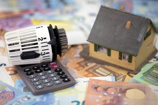 Heizungstausch mit finanziellen Zuschüssen Ein Spielzeughäuschen, ein Taschenrechner und ein Heizungsthermostat liegen auf Geldscheinen als Symbol für finanzielle Zuschüsse beim Gebäudeenergiegesetz