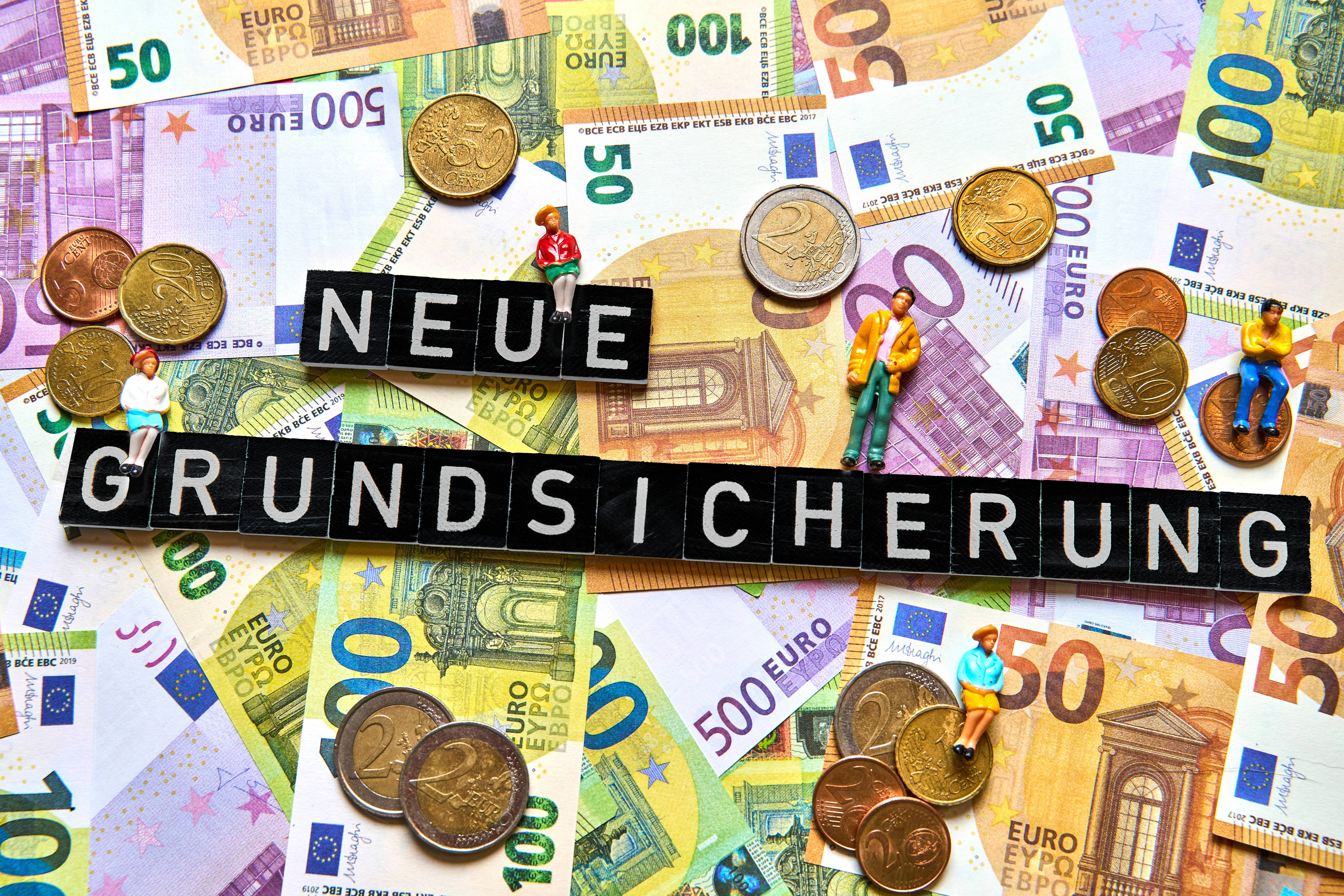 Geldscheine und M&uuml;nzen, darauf bilden Buchstabenw&uuml;rfel die Worte "Neue Grundsicherung"