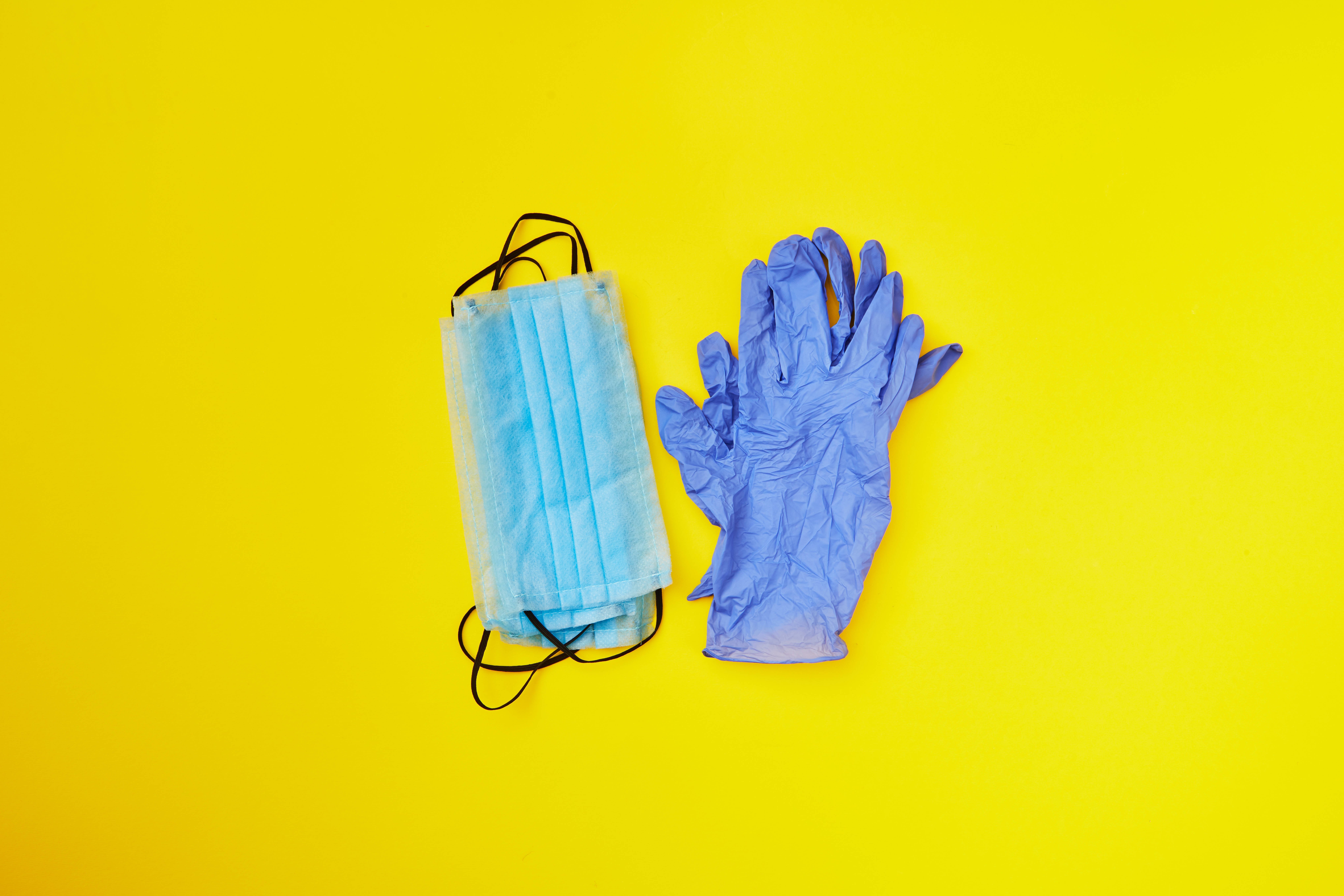 Hilfsmittel zum Verbrauch in der Pflege Blaue Einweg-Handschuhe und Mund-Nasen-Schutzmasken vor gelbem Hintergrund als Symbol für Hilfsmittel zum Verbrauch