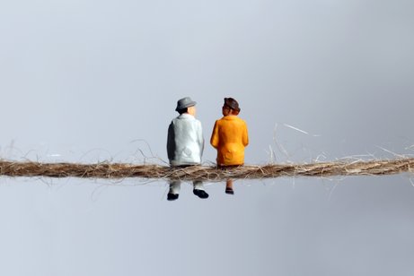 Zwei Mini-Fig&uuml;rchen eines &auml;lteren Mannes und einer &auml;lteren Frau sitzen nebeneinander auf einem d&uuml;nnen Seil mit dem R&uuml;cken zum Betrachter