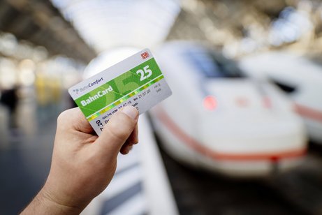 Bahncard 25 Eine Person steht an einem Bahngleis, an dem ein ICE der Deutschen Bahn steht, sie hält eine Bahncard 25 in der Hand.