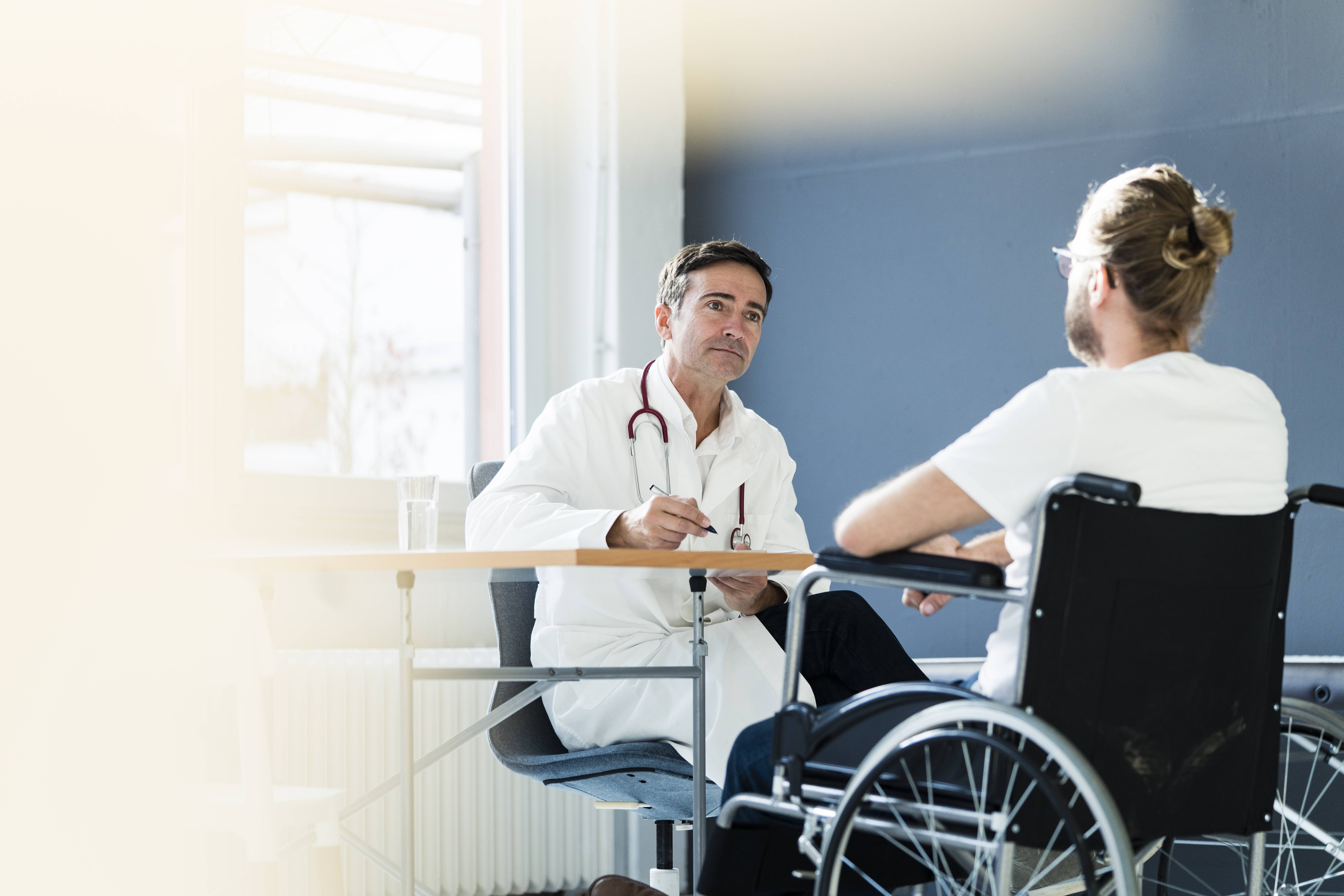 Arzt im Gespräch mit Patient im Rollstuhl Ein Mann im Rollstuhl sitzt einem Arzt gegenüber.