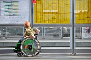 Mann im Rohlstuh studieet die Abfahrzeiten an einem Bahnhof