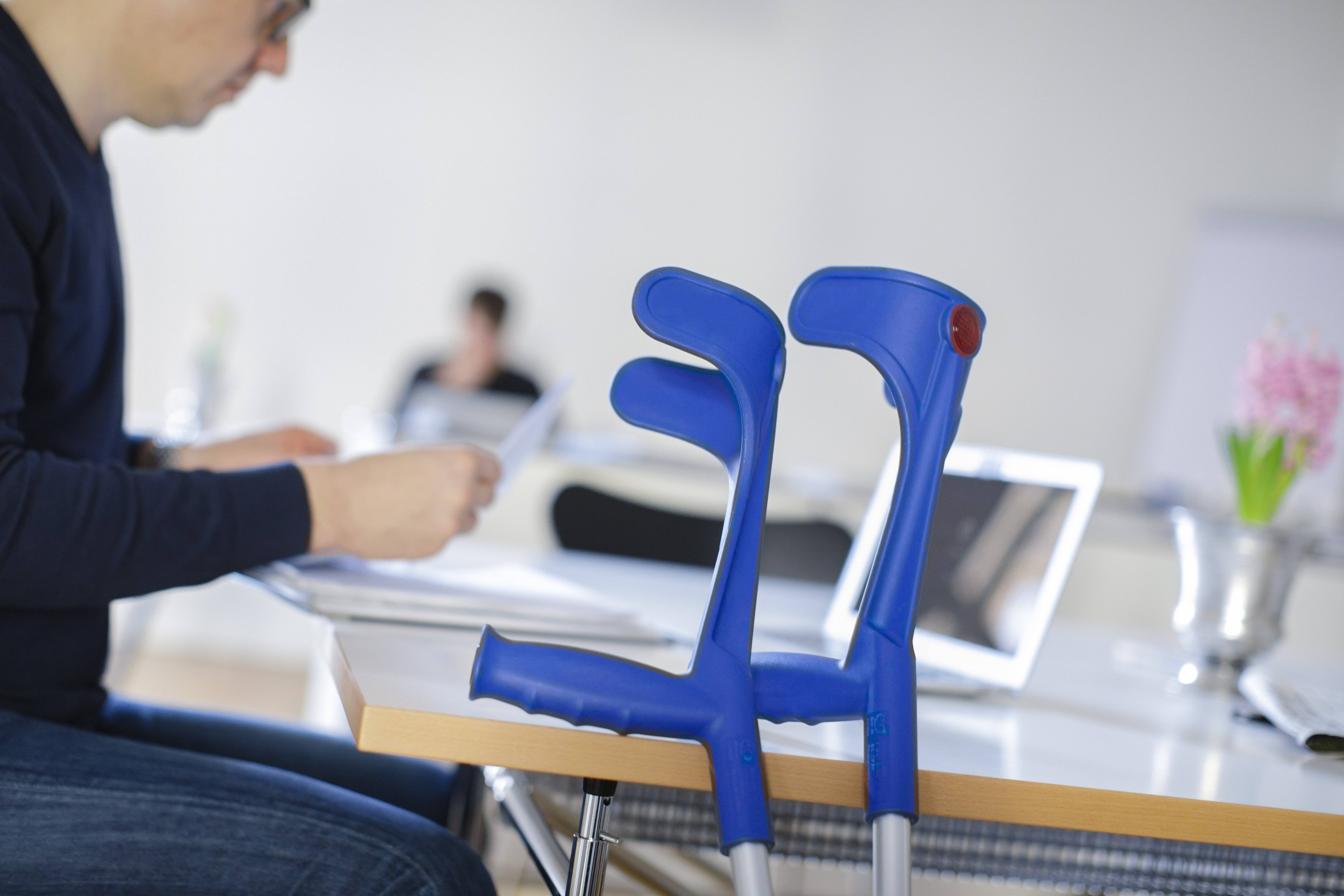 Ein Mann sitzt an einem Tisch, neben sich seine Krücken. 