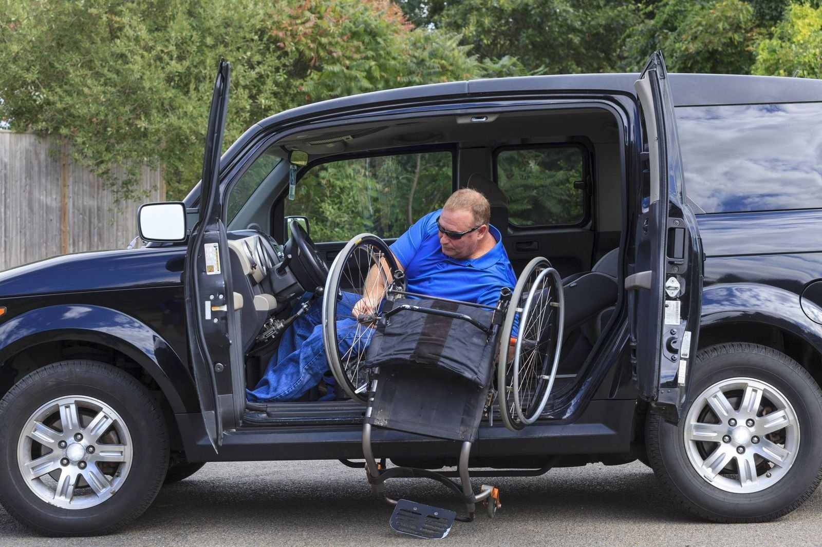 in Rollstuhlfahrer lädt seinen Rollstuhl aus einem behindertengerecht umgebauten Auto aus.