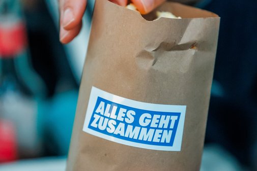 Jemand greift in eine Popcorn-Tüte, auf der das Logo der VdK-Aktion Alles geht zusammen klebt.