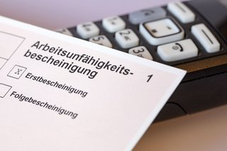 Eine Arbeitsunfähigkeitsbescheinigung mit einem Kreuz bei "Erstbescheinigung" und ein Telefon.