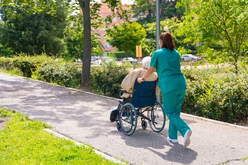 Krankenpflegerin schiebt alte Frau im Rollstuhl