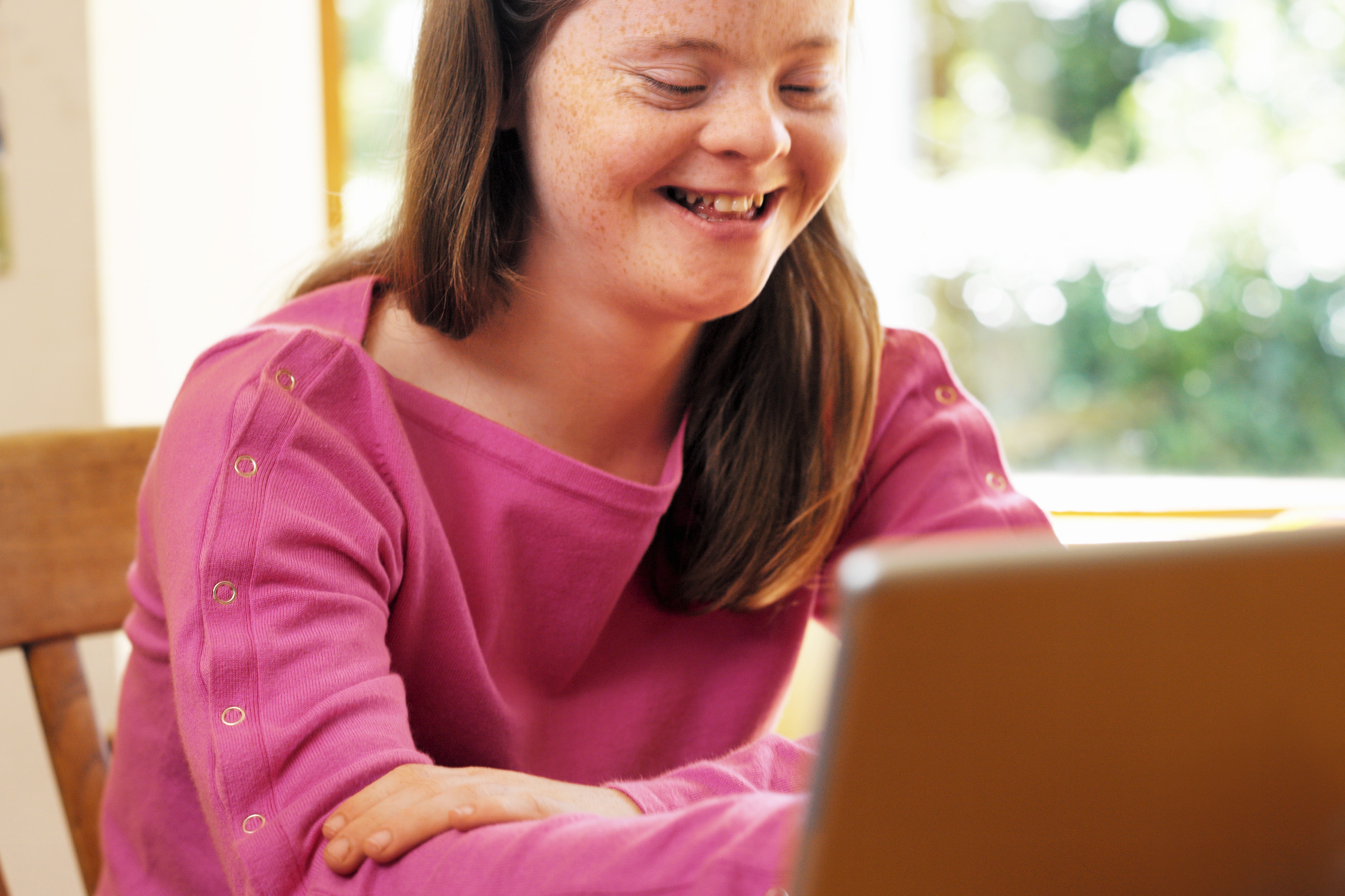 Eine junge Frau mit Downsyndrom sitzt an einem Tisch, vor sich ein aufgeklapptes Notebook.