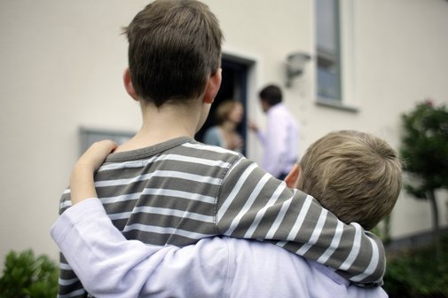 Scheidung und Unterhalt für die Kinder Zwei Jungen stehen Arm in Arm nebeneinander, im Hintergrund sieht man die Eltern streiten