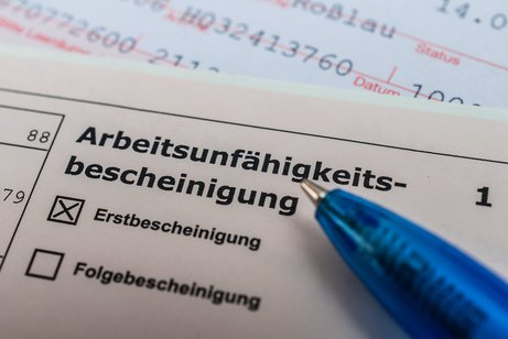 Eine Arbeitsunf&auml;higkeitsbescheinung, auf der "Erstbescheinigung" angekreuzt ist, darauf liegt ein Kugelschreiber