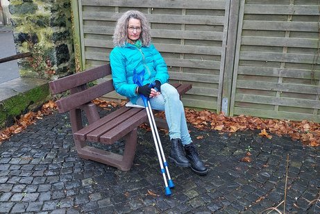 Tanja Gro&szlig; sitzt im Freien auf einer Bank, neben sich ihre Kr&uuml;cken.