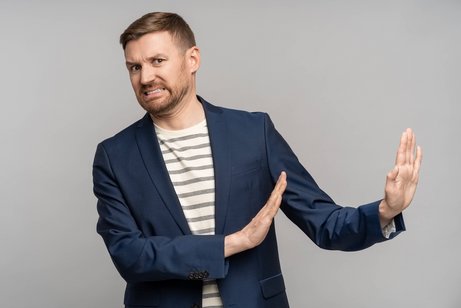 Ein Mann mit Abscheu im Gesicht macht eine abweisende Geste mit beiden Armen, er schiebt negativen Raum von sich weg.