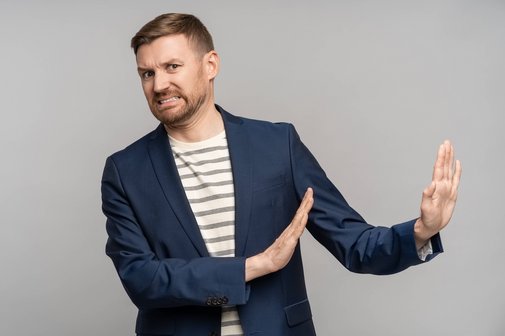 Ein Mann mit Abscheu im Gesicht macht eine abweisende Geste mit beiden Armen, er schiebt negativen Raum von sich weg.